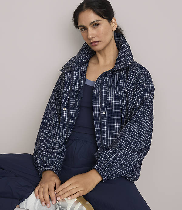 A woman in a navy checkered jacket and matching pants sits against a plain, light gray background.