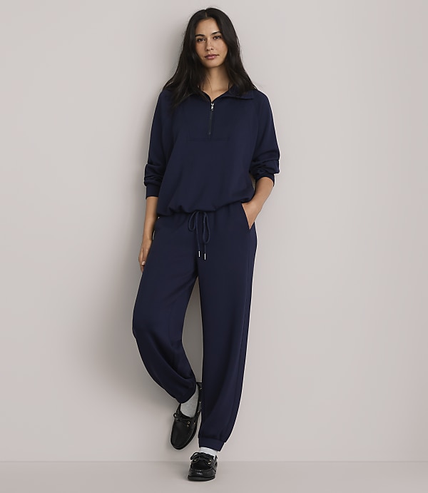 A woman in a navy blue tracksuit stands against a plain, light-colored wall.