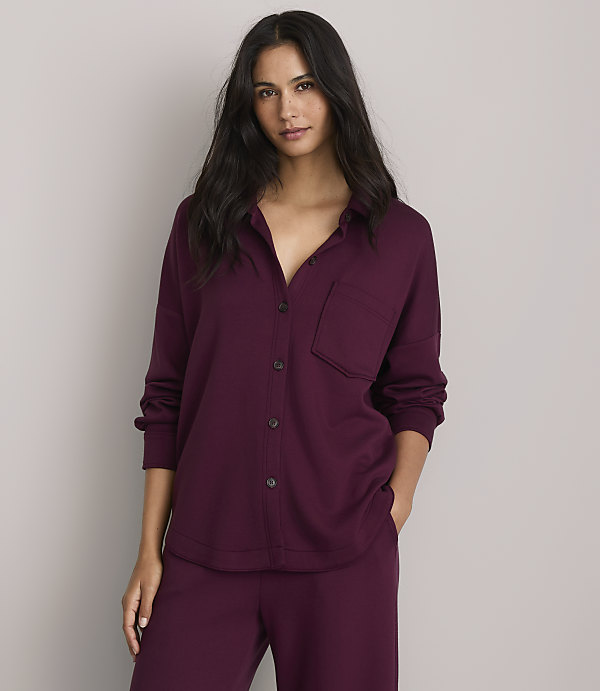 A woman in a burgundy pajama set stands against a plain gray background.