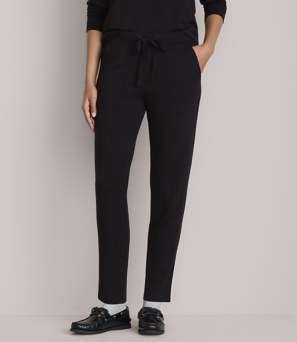 A person wearing black drawstring pants and black shoes stands against a plain gray background.