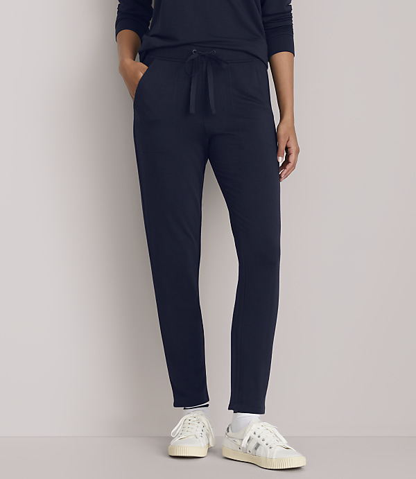 A person in navy blue loungewear and white sneakers stands against a plain, light gray background.