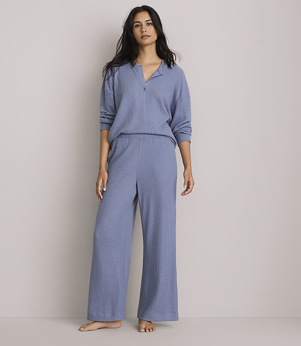 A woman stands in a light blue waffle-knit pajama set against a plain, light gray background.