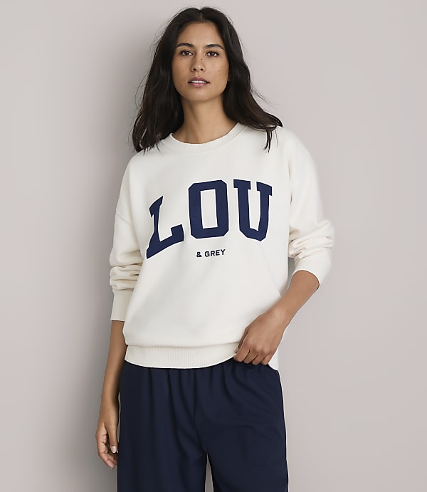 A woman in a cream sweatshirt with "LOU & GREY" printed on it stands against a plain, light gray background.