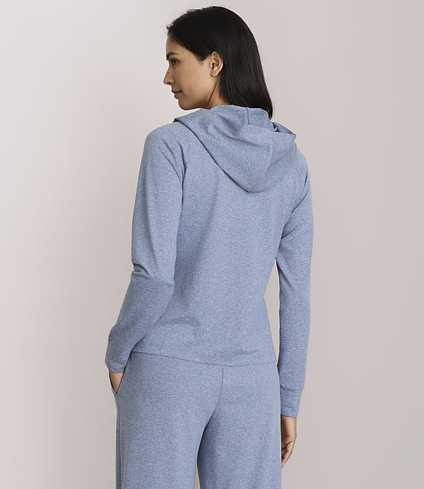 A woman in a blue hoodie and pants stands against a plain, light pink background.