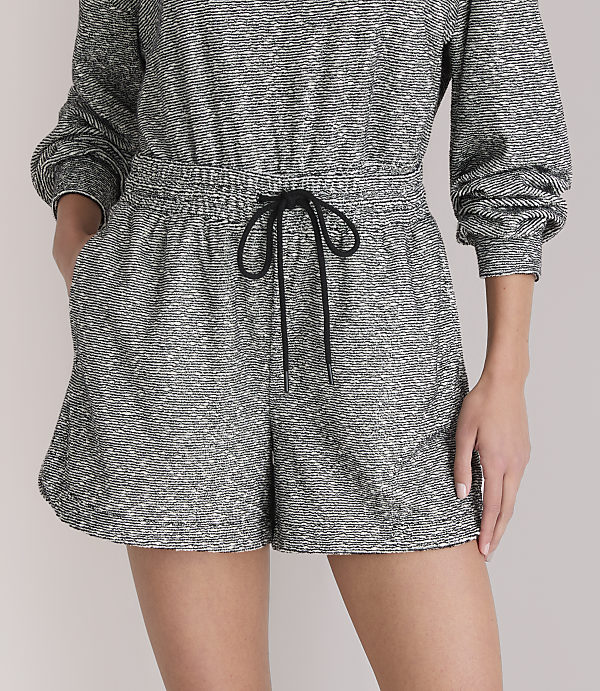 A person models a grey and white patterned romper with a black drawstring in the foreground, against a plain white background.