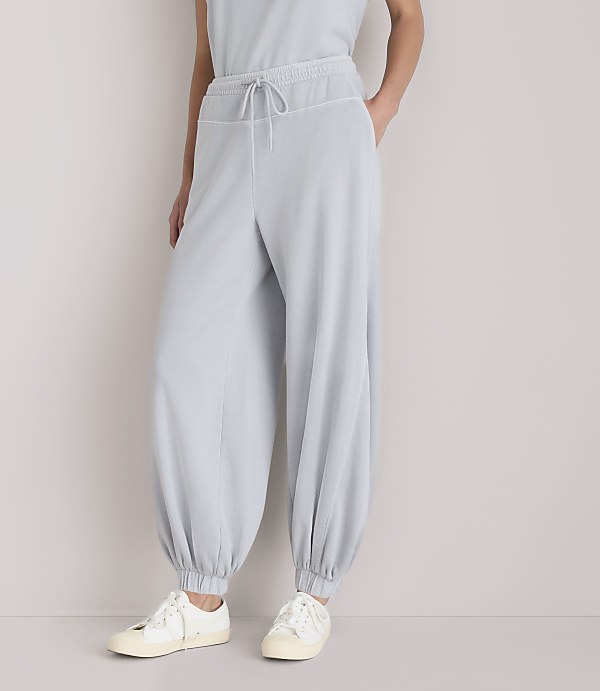 A person stands in light gray, baggy pants and white sneakers against a plain white background.