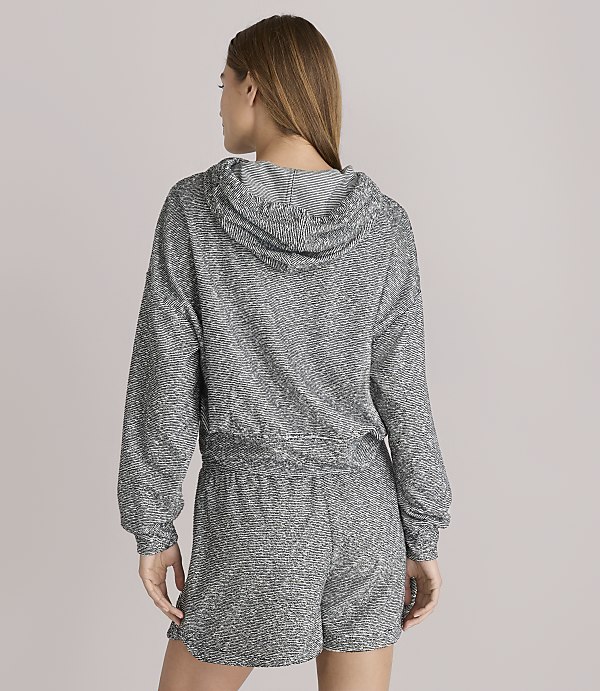 A woman in a sparkly grey hoodie and shorts stands against a plain white background.