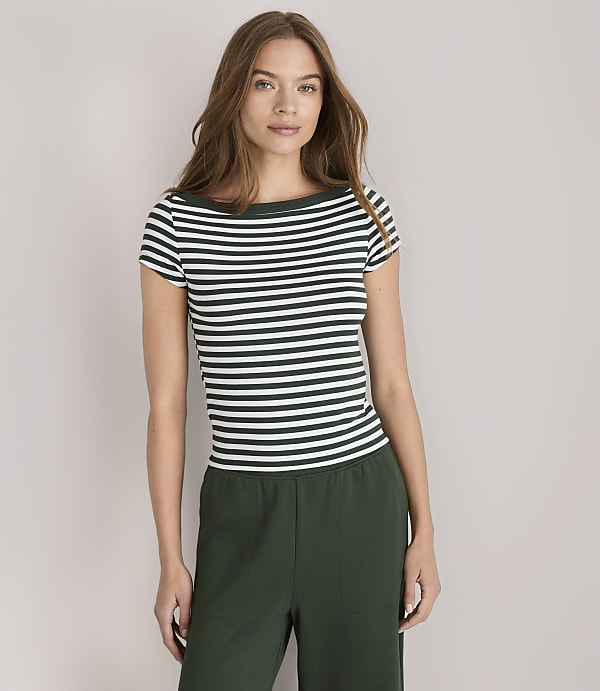 A woman in a striped shirt and green pants stands against a plain white background.