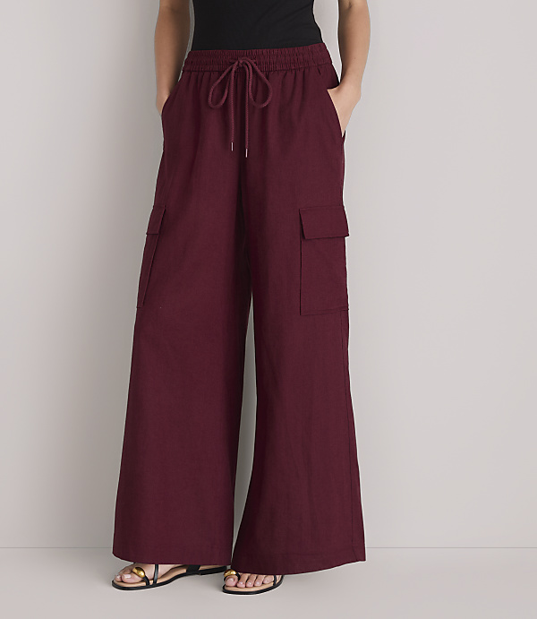 A person stands in front of a plain white background, wearing loose-fitting maroon cargo pants with their hands in their pockets.