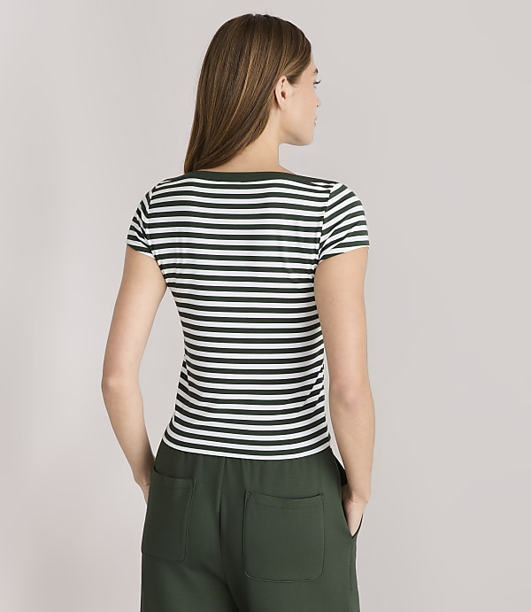 A woman in a striped t-shirt and green pants stands against a plain gray background.