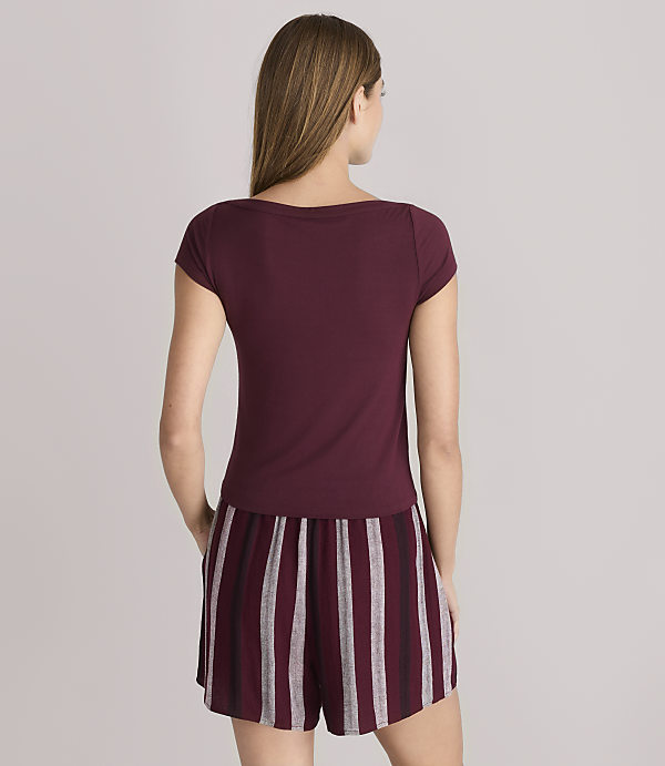 A woman in a maroon t-shirt and striped shorts stands against a plain gray background.
