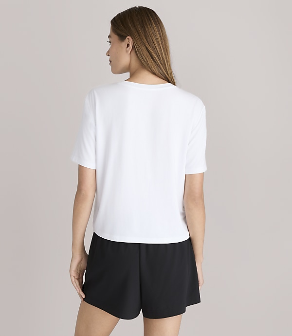 A woman in a white t-shirt and black shorts stands against a plain white background.