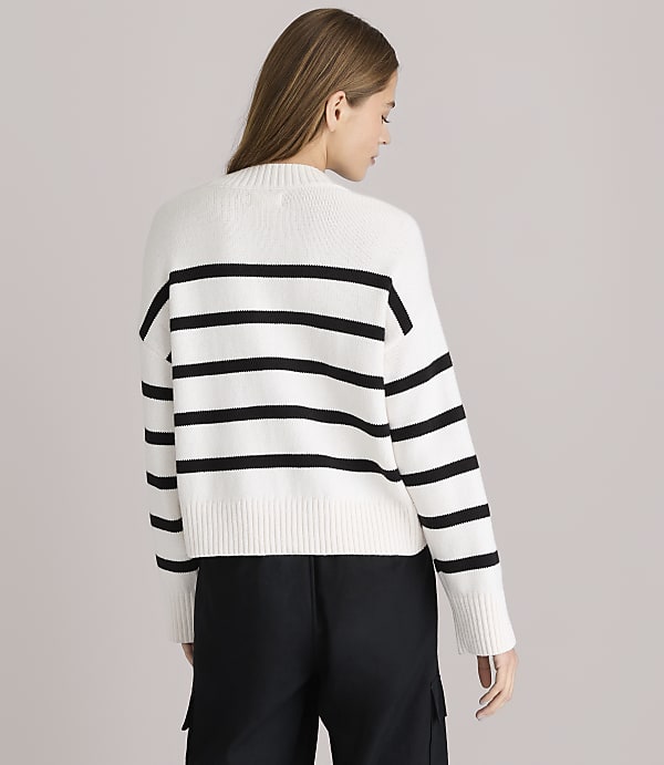 A woman in a white and black striped sweater stands against a plain white background.