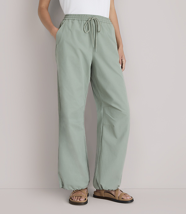 A person stands in light green pants with a drawstring waist and sandals, against a plain white background.