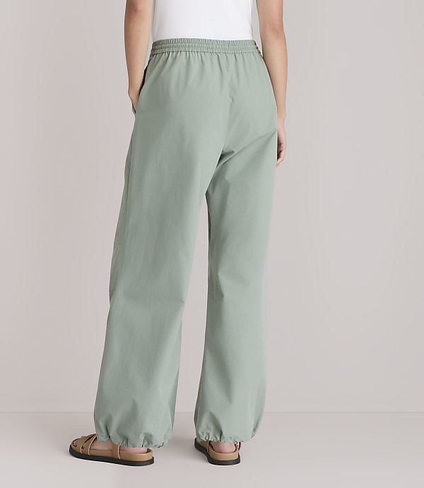 A person wearing loose-fitting, light green pants with elastic cuffs stands with their back to the camera against a plain white background.