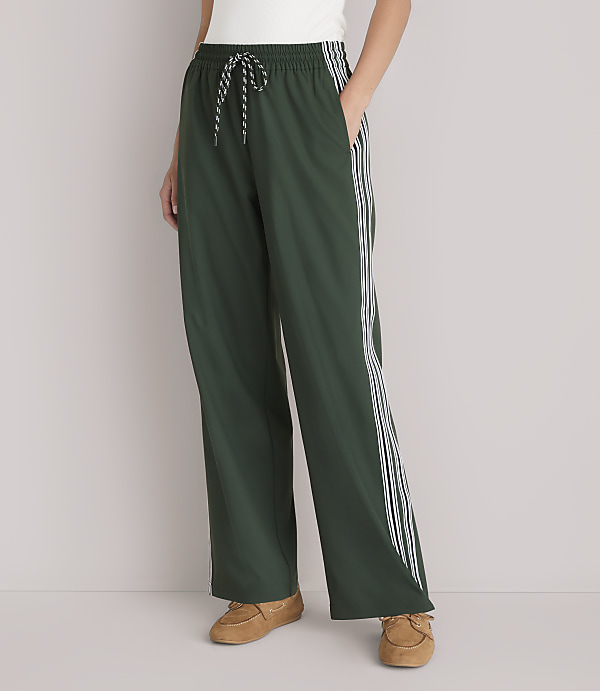 A person stands in dark green athletic pants with white stripes down the sides, wearing brown loafers against a plain white background.