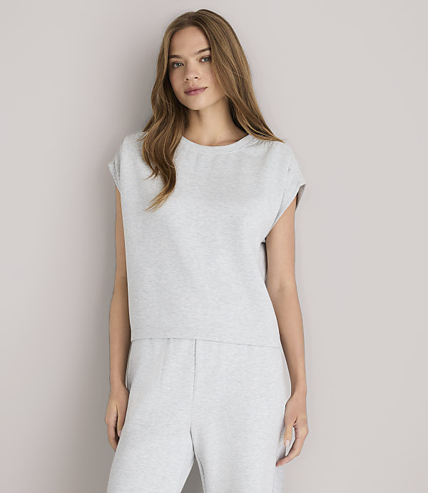 A young woman in a grey loungewear set and white sandals poses against a plain grey background.