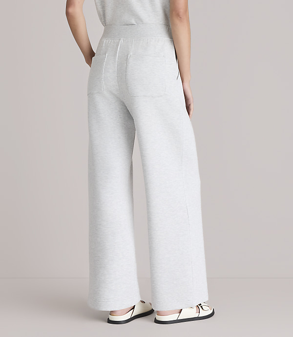A person wearing light gray wide-leg sweatpants and white sandals stands against a plain white background.