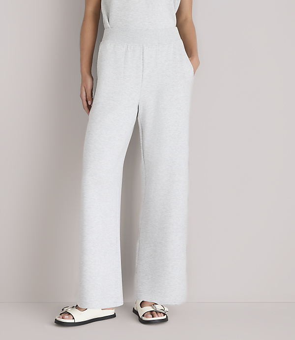 A person wearing light gray wide-leg sweatpants and white sandals stands against a plain white background.