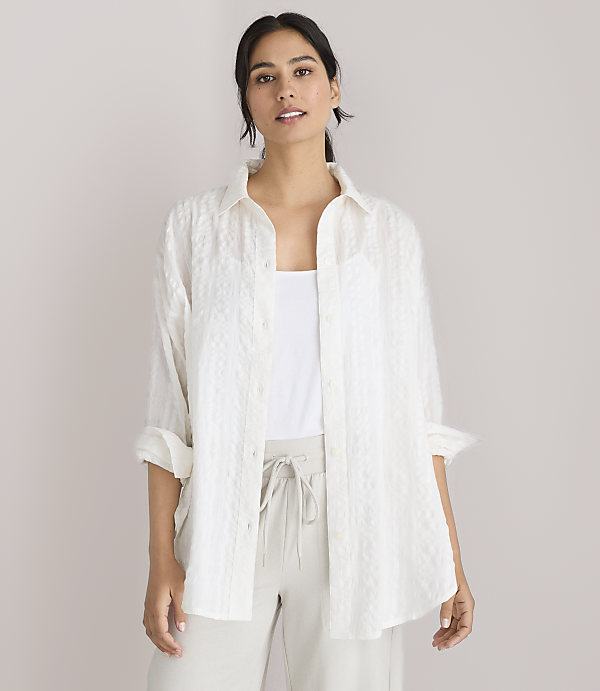 A woman in a white textured shirt and light-colored pants stands against a plain white background.
