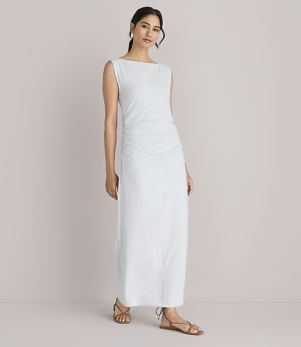 A woman in a light-colored, ruched maxi dress stands against a plain white background.
