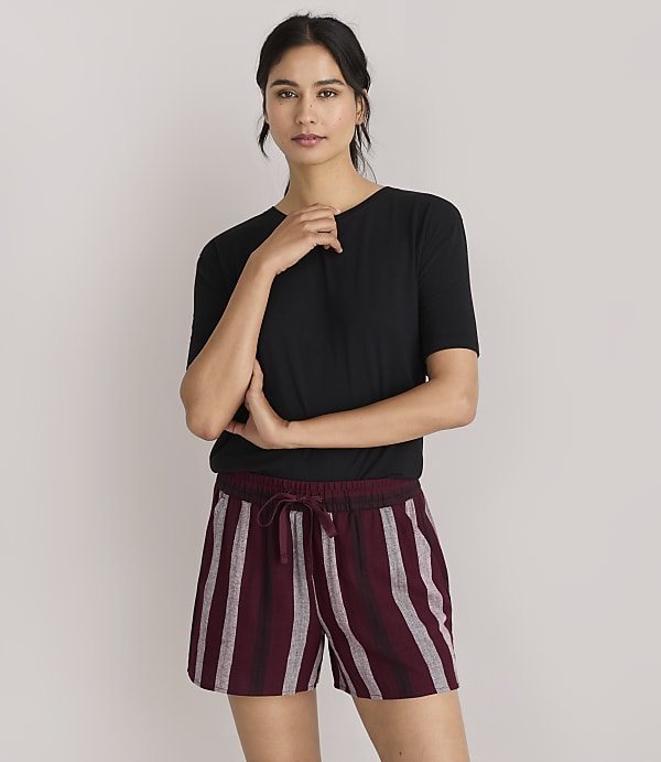 A woman in a black t-shirt and striped shorts stands against a plain white background.