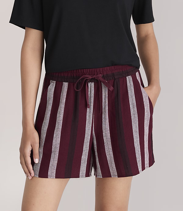 A person in a black t-shirt and striped burgundy shorts stands against a plain white background.