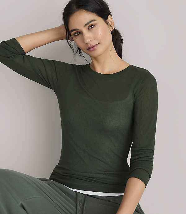 A woman in a green sweater and pants stands against a plain gray background.