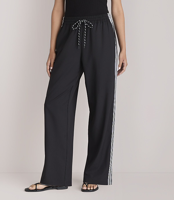 A person stands in black wide-leg pants with white stripes down the sides, against a plain white background.