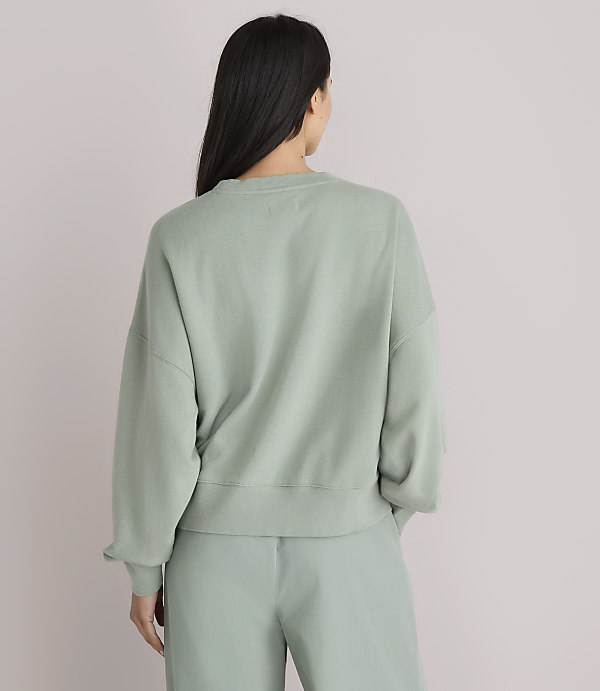 A woman in a light green sweatshirt and pants stands with her back to the camera against a plain white background.