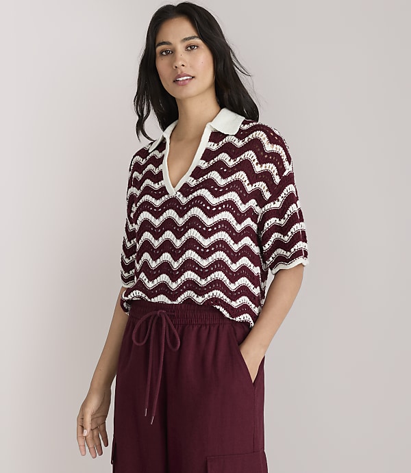 A woman in a chevron-patterned top and maroon wide-leg pants stands against a plain white background.