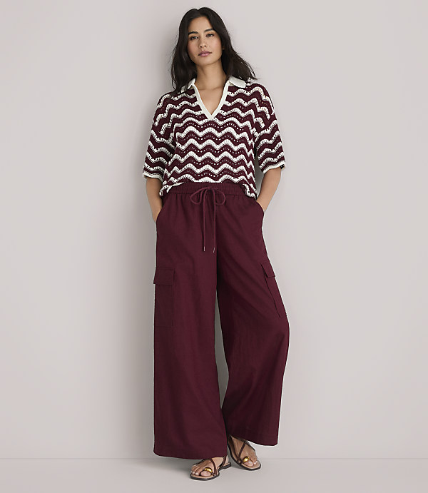 A woman in a burgundy and white chevron-patterned knit polo shirt and burgundy pants stands against a plain white background.