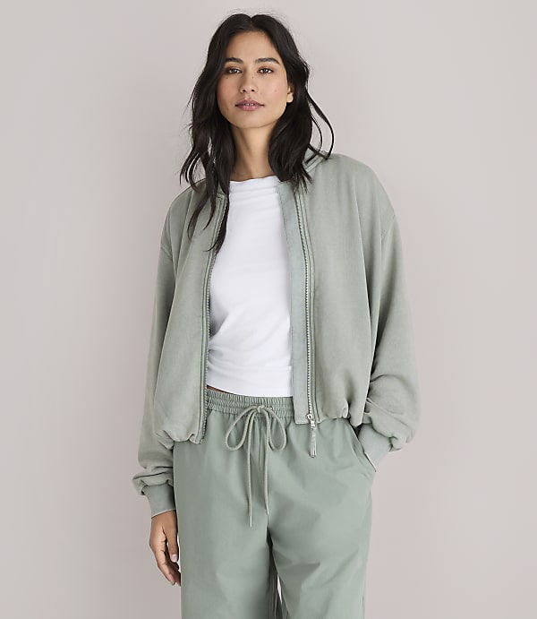 A woman in a light green bomber jacket and matching pants stands against a plain white background.