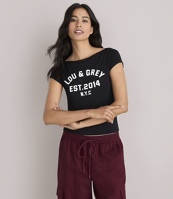 A woman in a black "LOU & GREY EST. 2014 N.Y.C." t-shirt and maroon cargo pants stands against a plain white background.