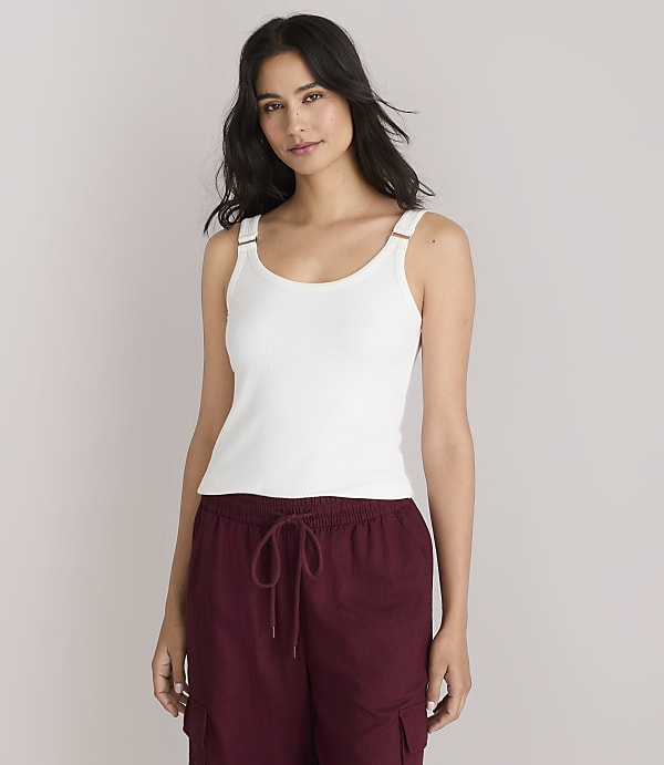 A woman in a white tank top and maroon pants stands against a plain white background.