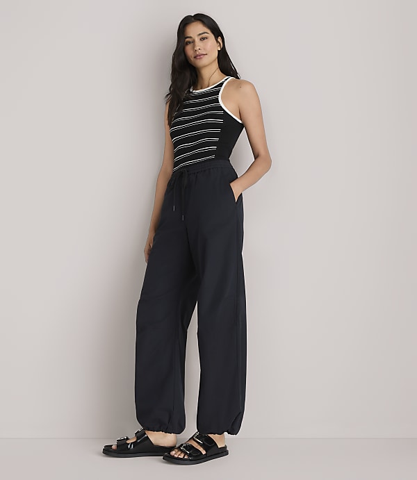 A woman in a striped tank top and baggy pants stands against a plain white background.