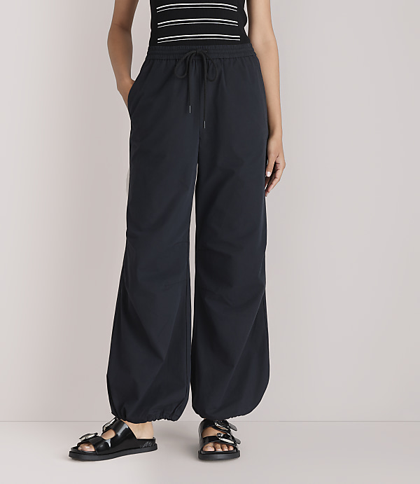 A person stands in black balloon pants and sandals against a plain white background.