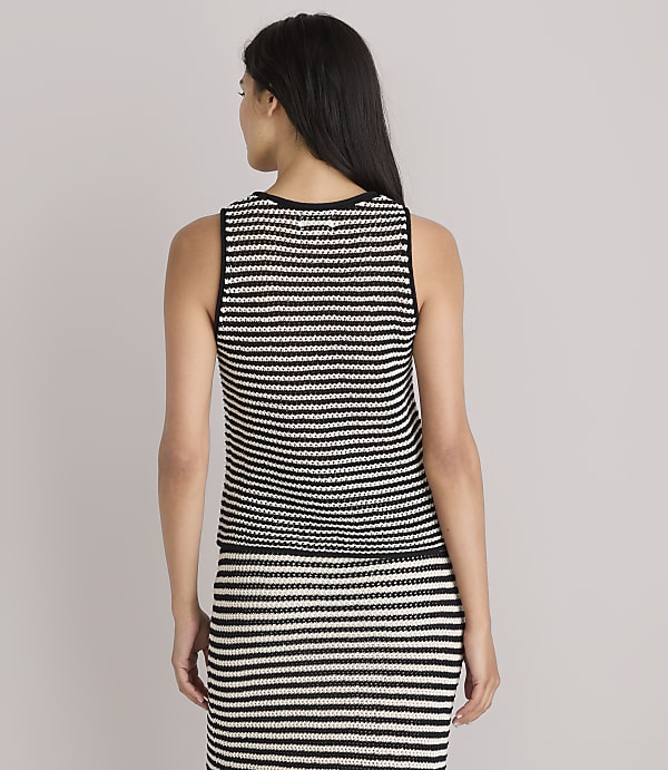 A woman in a striped tank top and skirt stands against a plain white background.