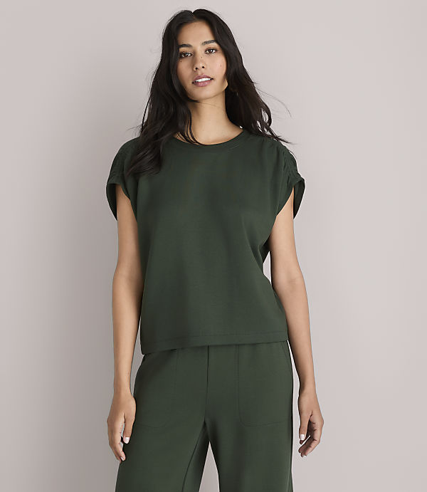 A woman in a dark green top and pants stands against a plain white background.