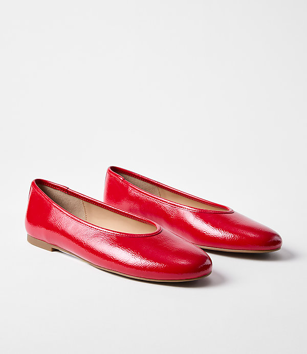 A pair of shiny red ballet flats rests on a plain white background.