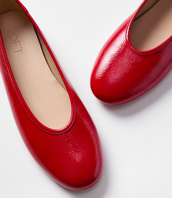 Two shiny red ballet flats are arranged on a white background.