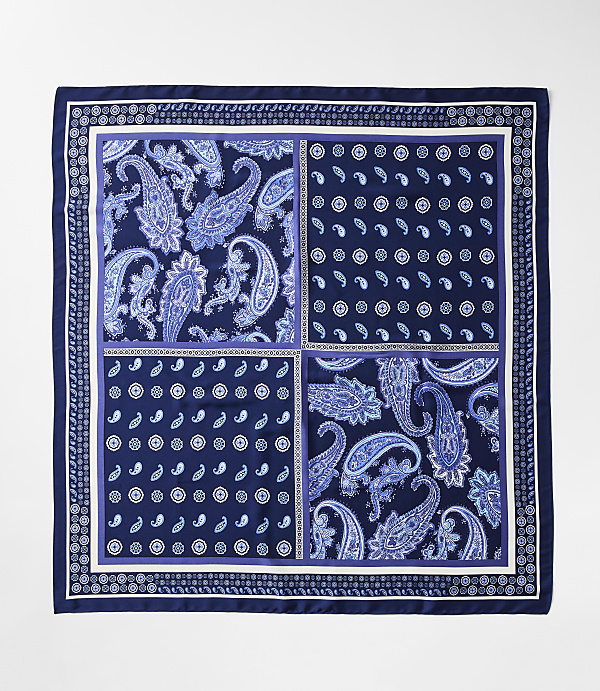 A square silk scarf with a dark blue border features four distinct quadrants of paisley and floral patterns in shades of blue and white, set against a plain white background.