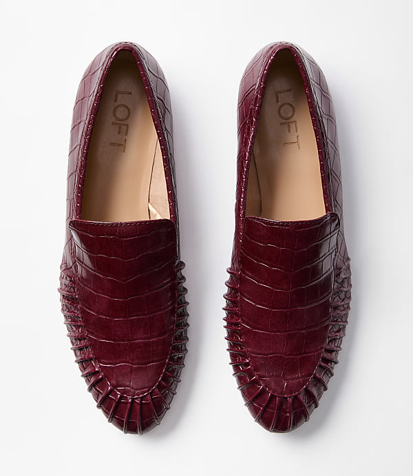 A pair of burgundy embossed loafers with ruffled detailing are laid flat against a plain white background.