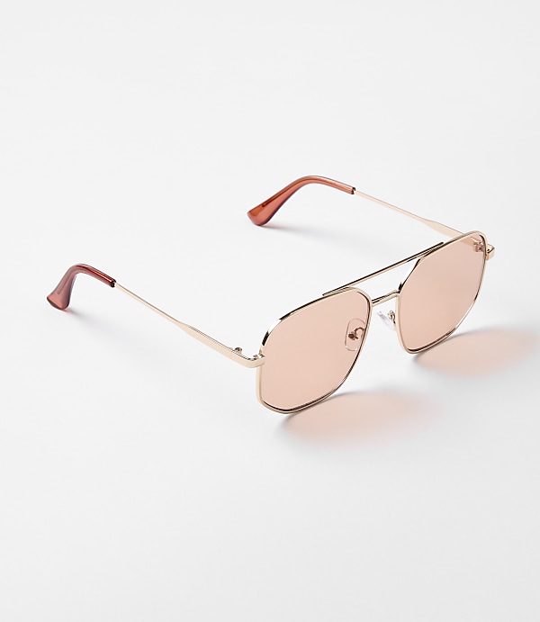 A pair of rose-gold aviator sunglasses with pink lenses rests on a plain white surface.