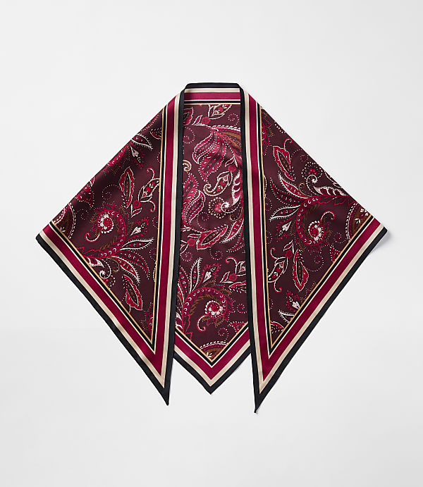 A maroon paisley-patterned silk scarf with a black and cream border lies flat against a plain white background.