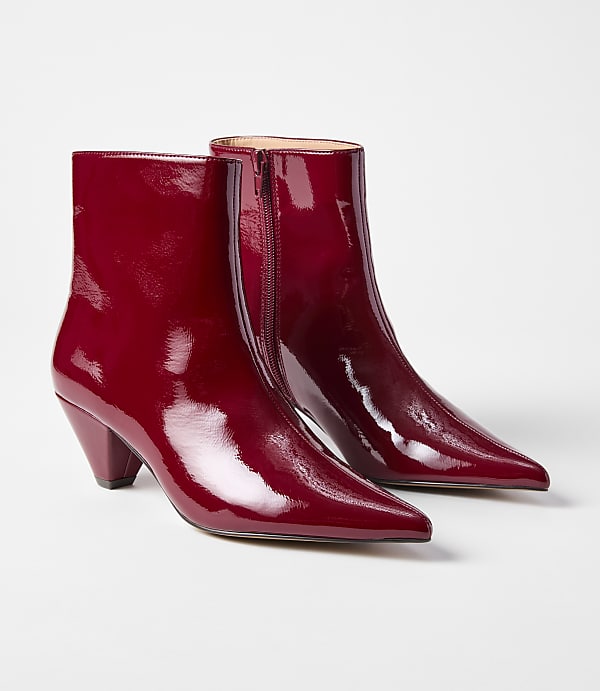 A pair of glossy red pointed-toe ankle boots with block heels rests on a plain white background.