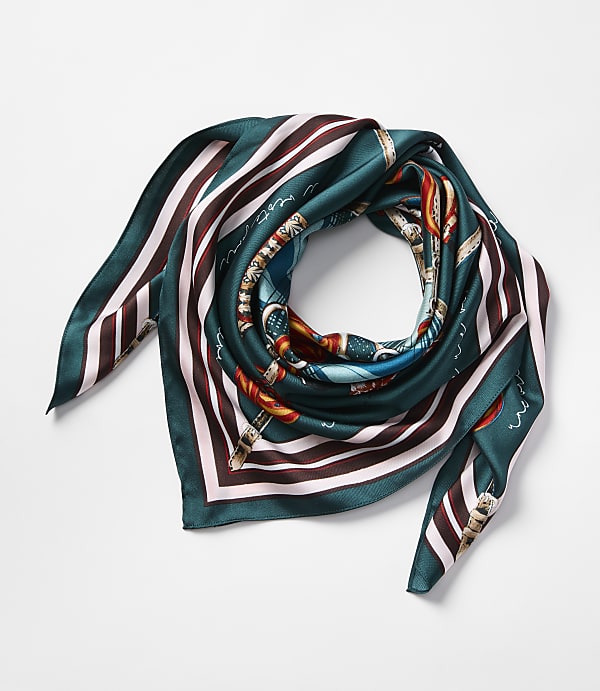 A folded silk scarf with a dark teal, brown, and cream striped border and a central equestrian print rests on a plain white background.