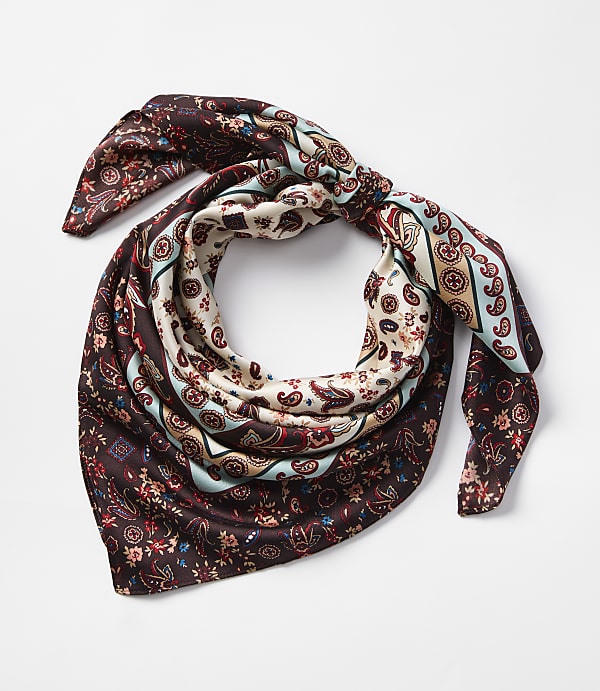A patterned silk scarf with paisley and floral designs is tied in a knot against a plain white background.