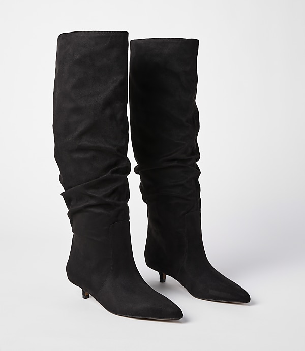 A pair of black slouchy suede boots with pointed toes and kitten heels stand against a plain white background.