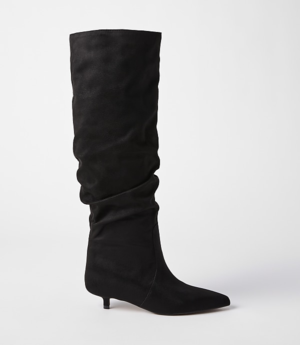 A black slouchy suede boot with a pointed toe and kitten heel stands against a plain white background.
